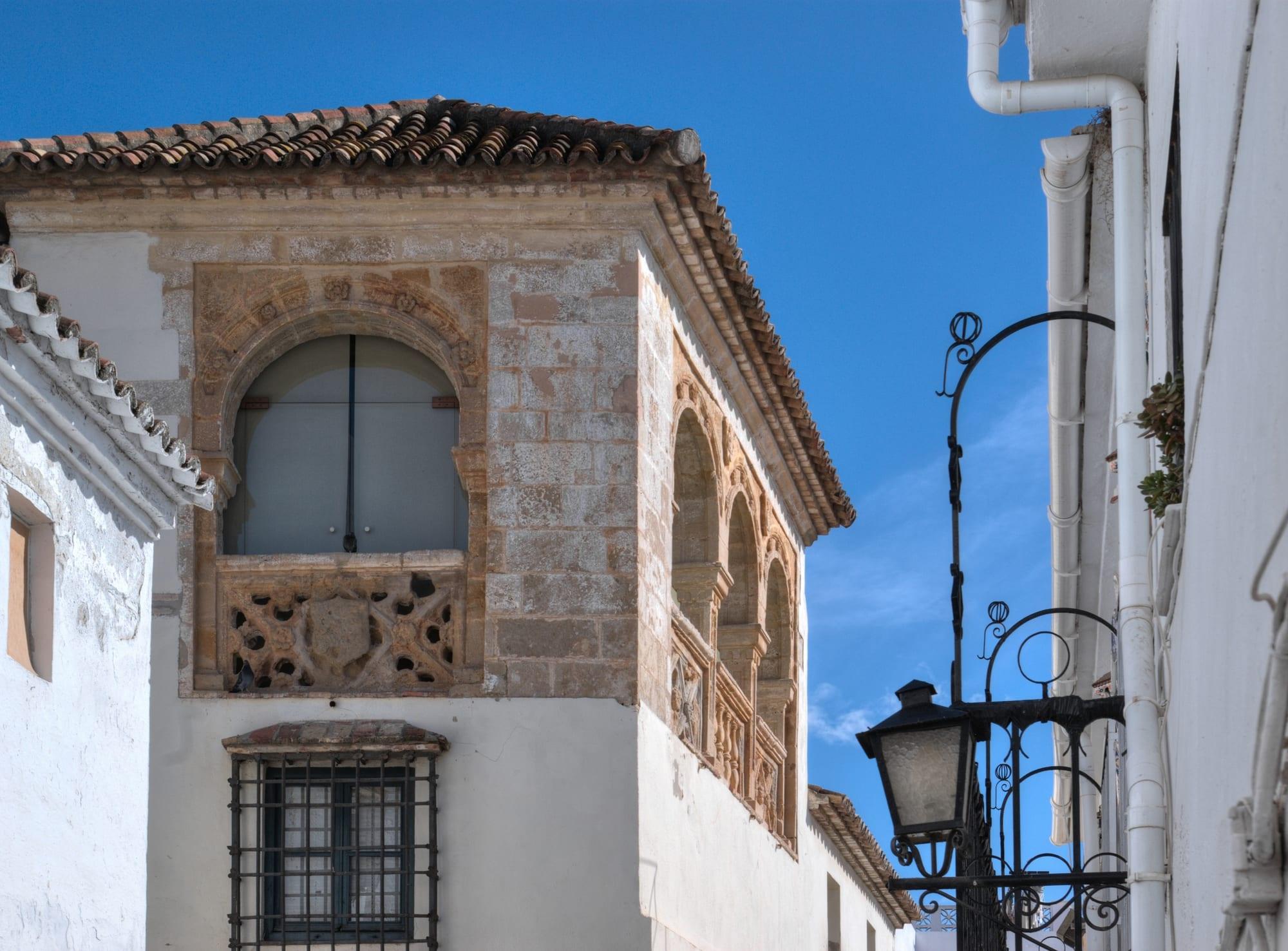 Carved stone arched window and Renaissance gallery on the whitewashed old Hospital Bazán, now the Museo del Grabado Español, beside a wrought-iron street lamp